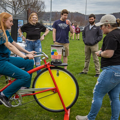 Megan Marie Foley, a second-year dental hygiene student from Clarendon, uses pedal power to whip up a bicycle smoothie. Among those cheering on the process is robotics student Lauryn A. Stauffer (right foreground), WEB's Wildcat Wednesday team lead.
