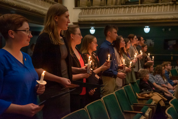 Alpha Chi inductees return to their seats, the warm glow of candlelight infusing the auditorium.