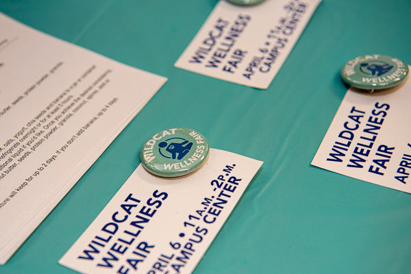 Wildcat Wellness Fair pins are offered on a table.