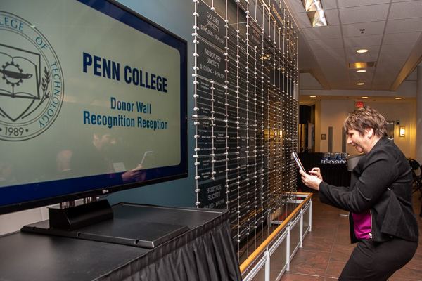 Dorothy Minnick – the wife of alumnus Howard C. Minnick Jr., whose Automation Systems Interconnect Inc. was welcomed into the Heritage Society – takes a cellphone photo of the Donor Wall.