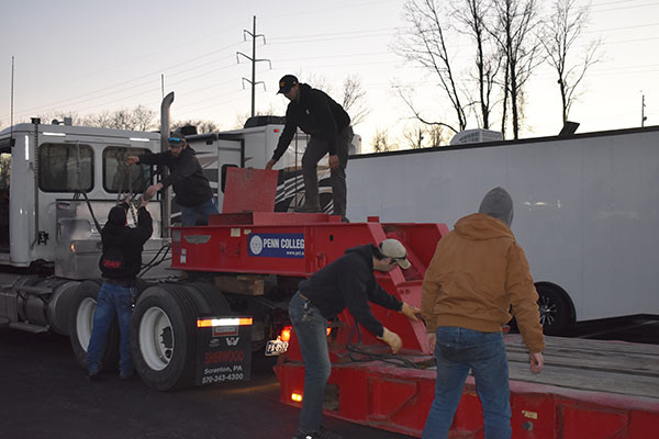 Setting up the lowboy: From left, Solly is handed chains by Biehl, and Spinosa takes chains from an upper compartment. At ground level are Seth J. Welshans, laboratory assistant for diesel equipment technology, and Brubaker (to his right).