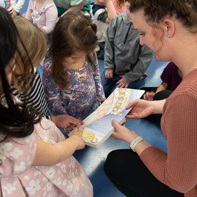 Children – with the help of Valerie L. Vonada, an assistant group leader – feel the Braille lettering in one of Mason’s books, shared by Rogers for the event.