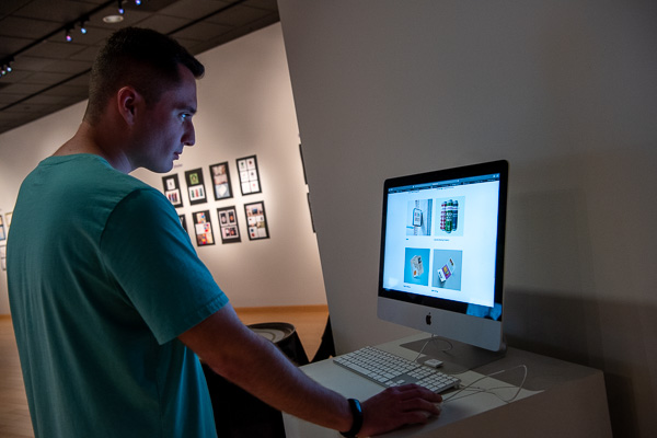 Glowing in the light of technology, a visitor considers designs displayed on an iMac.