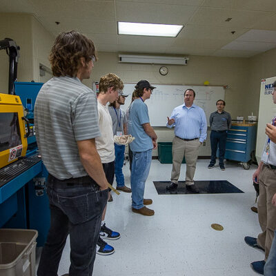 In a plastics lab, the acting secretary converses with young visitors and faculty about their experiences so far. Among those sharing insight are Mark A. Sneidman (left) and Joshua R. Rice (background, behind Weaver), instructors of plastics technology.