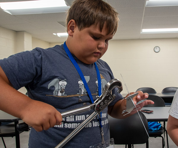 While learning about aviation maintenance, a participant adds a rivet to a metal model airplane.