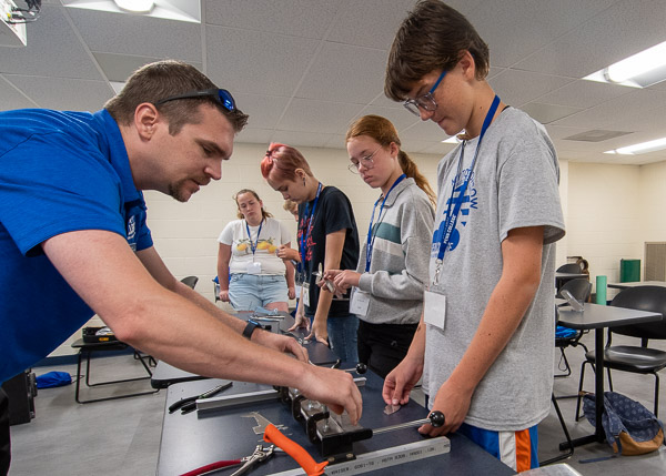 Matthew D. Krepps, instructor of aviation maintenance, demonstrates how to use a metal brake to bend pieces of a metal airplane model into shape.