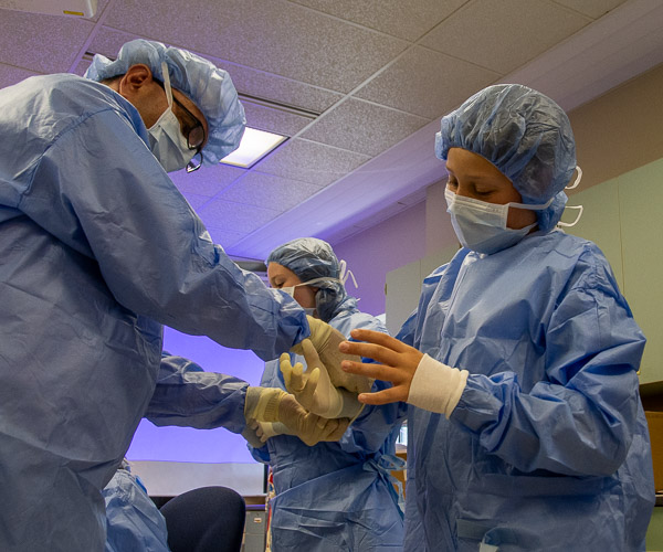 After a thorough hand (and arm) scrub, the last step is to get gowned and gloved – with help from Scott A. Geist (left), director of surgical technology.