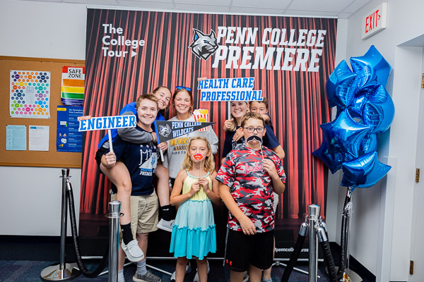 Mangene (left foreground) – softball player; heating, ventilation & air conditioning design technology student; and one of the stars of the video tour – livens up the ACC photo booth just beyond the ceremonial blue carpet.