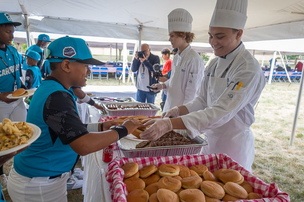 Athletes from Willemstad, Curacao – the Caribbean entry – move through the food line, where dogs, burgers, and mac 'n' cheese are (as ever) popular fare.