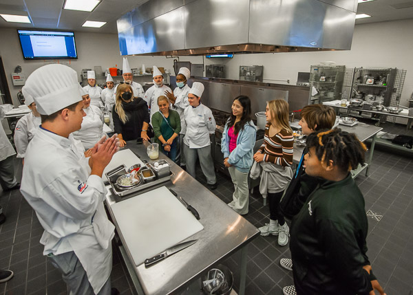 Kade N. Chrostowski (foreground), of Moorestown, N.J., majoring in culinary arts technology and applied management, tells the lab guests about the previous day's assignment: a chicken dish with a prep-to-plate deadline of two hours and 15 minutes. He is among the students in the Foundations of Professional Cooking course taught by Chef Frank M. Suchwala (center background), associate professor of hospitality management/culinary arts. 