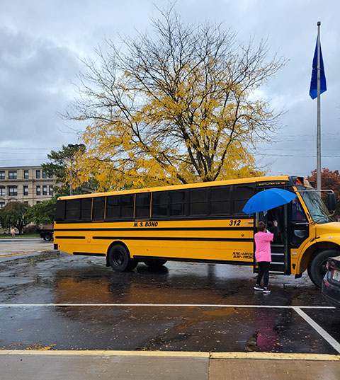 A staff volunteer, designated by her pink shirt, greets a bus pulling into campus.