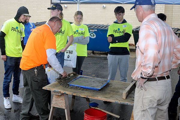 Montoursville Area High School students enjoy watching their chaperone smooth out a section of concrete. Overseeing the trowel work is Harry W. Hintz Jr., instructor of construction technology, and one of the faculty members who volunteered at the start of their Fall Break to guide prospective future students.