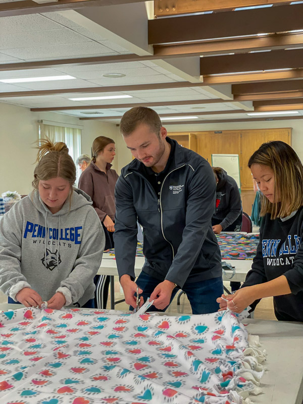 Martinez, Wolf and Smith cut fringe and tie it to construct a fleece blanket that will be donated to a hospital or other organization to provide comfort to a child.