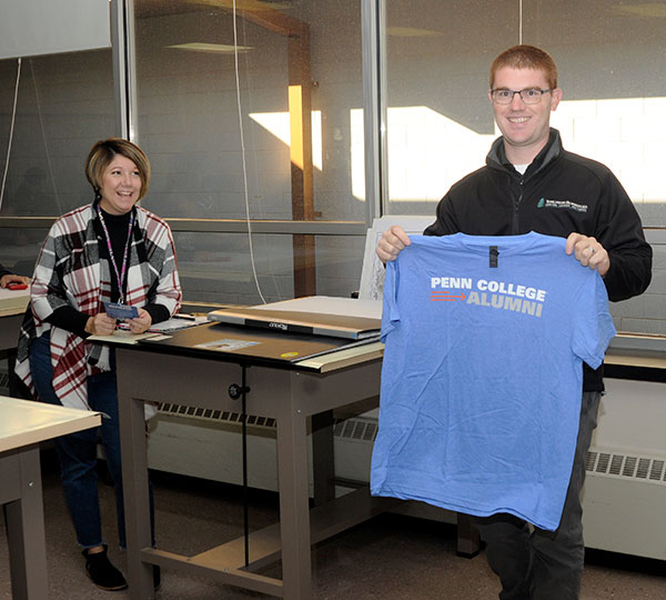 ... and was presented with a Penn College Alumni T-shirt by Lori A. Boos (left), alumni and career engagement coordinator, and Shelley L. Moore (not pictured), senior director of the Center for Career Design.