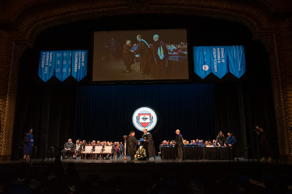 Reed and Steven P. Johnson (right), a member of the Penn College Board of Directors, award degrees and certificates, their work made visible on an overhead screen. At left, Carolyn R. Strickland, vice president for enrollment management and associate provost, reads each graduate's name.