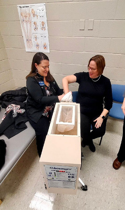 Snyder-Everitt (left) allows Myra K. Shaffer, college relations and foundation assistant, to try out the program’s fluidotherapy unit, which circulates heat and increases blood flow around sore joints.