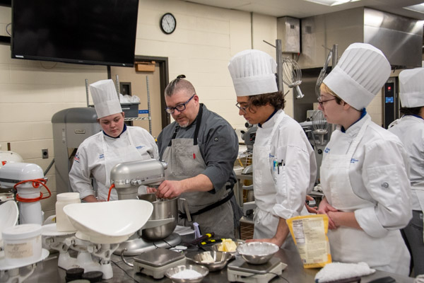 Chef Brian Doyle, ’94, troubleshoots a formula with students (from left) Sydney L. Mahoney, of Roaring Spring; Christopher J. Macdonald, of Emmaus; and Emily E. Kohen, of Mill Hall.