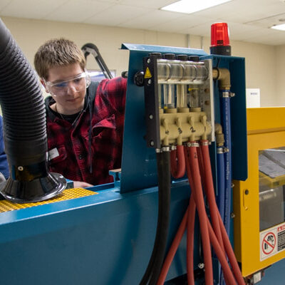 A Warrior Run student works to remove purged material from an injection molder.