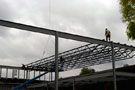 Workers deftly traverse steel beams, as another truss is lowered into place for the addition to the ATC