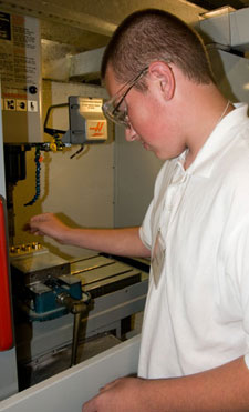 A camper loads brass checkers into a Haas Super Mini Mill for engraving in Pennsylvania College of Technology's Automated Manufacturing Lab.