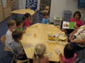 Children gather 'round the table to hear Laura Tanner