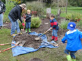 Children shovel soil over their planted daffodil bulbs