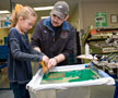 A young visitor works with David L. Weaver, a graphic communications management student from Williamsport, on the screen-printing carousel