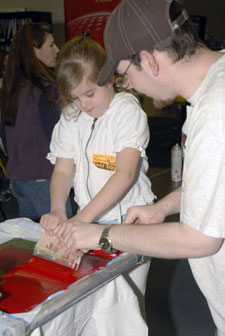 Penn College student David L. Weaver, president of Gamma Epsilon Tau, a graphic arts honors fraternity, helps a Lyter Elementary School first-grader screen-print a T-shirt in one of the college%E2%80%99s graphic communications labs.