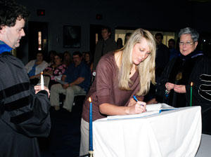Jessica R. Larson signs the Alpha Chi constitution, as faculty sponsor Gerald 'Chip' Baumgardner holds her candle and President Davie Jane Gilmour waits with her membership pin.
