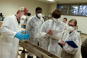 Pennsylvania College of Technology student Bradley J. Stroup, left, explains the process of twin-screw compounding to a group of Penn State nanofabrication manufacturing technology students as Penn College students produce samples of a polymer-based nanocomposite for the Penn State group.