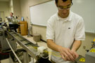 A student feeds long strands of plastic material from an extruder to a machine that will dice it into pellets.