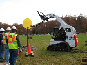As industry judges watch at left, a Precision Heavy Construction Equipment Rodeo competitor uses a skid steer to score some unconventional  %E2%80%9Clay-ups%E2%80%9D at Pennsylvania College of Technology%E2%80%99s Schneebeli Earth Science Center.