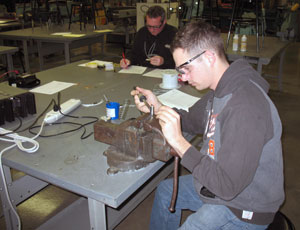 Neil F. Baughman solders wires onto a connector while judge Brett A. Reasner scores a previously completed project during Tuesday's SkillsUSA aviation competition at Pennsylvania College of Technology's Lumley Aviation Center in Montoursville. (Photo by Thomas D. Inman, associate professor of avionics)