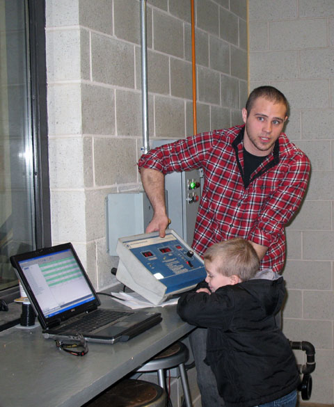 Student volunteer Ethan P. Jandreau, a diesel technology major, explains the ESC dynamometer room from the control booth (with the help of a young friend).