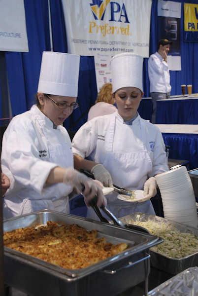 Angela Snyder and Rachel Emmons, both enrolled in culinary arts and systems, serve samples near the Culinary Connection stage.