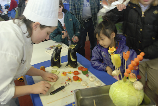 Tiana Soles-Ahner, a baking and pastry arts major, carves vegetables for a curious onlooker.