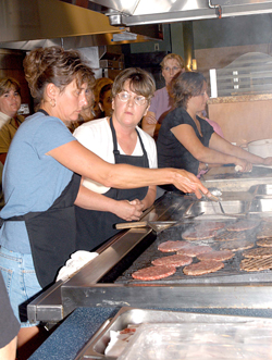 Ann Seeley (center) shows Food Services employee Kathy L. Bozochovic (left) how to cook patties made from grass-fed beef.