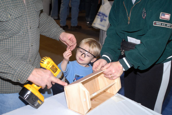 A young carpenter-in-training hands a wood screw to his mentor at the School of Construction and Design Technologies exhibit.