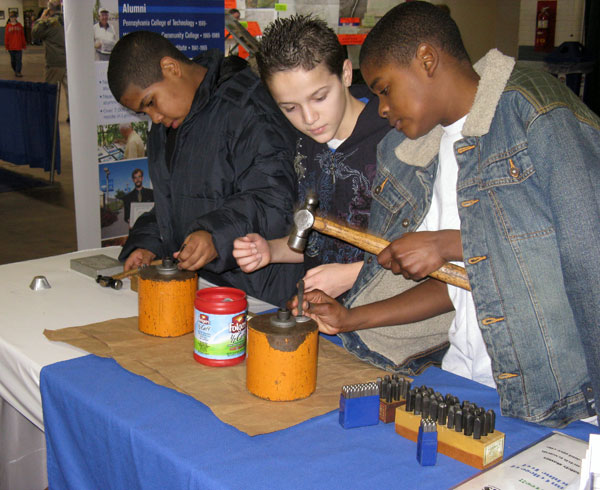 Visitors to the School of Industrial and Engineering Technologies display use hammers to stamp ID tags, some of which were used for pets and some as keychains or necklaces.