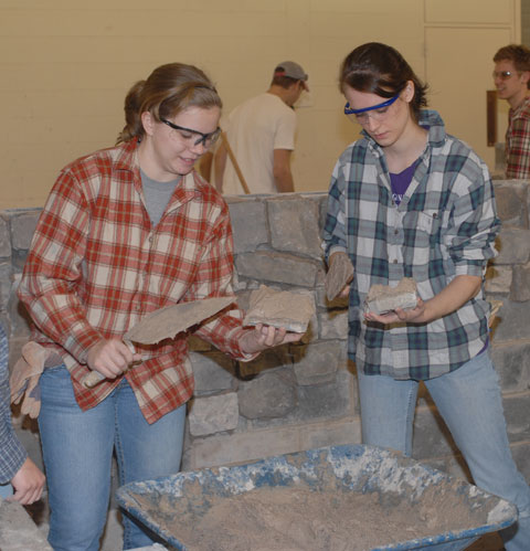Penn State students apply mortar to natural stone prior to adding their touch to the wall behind them.
