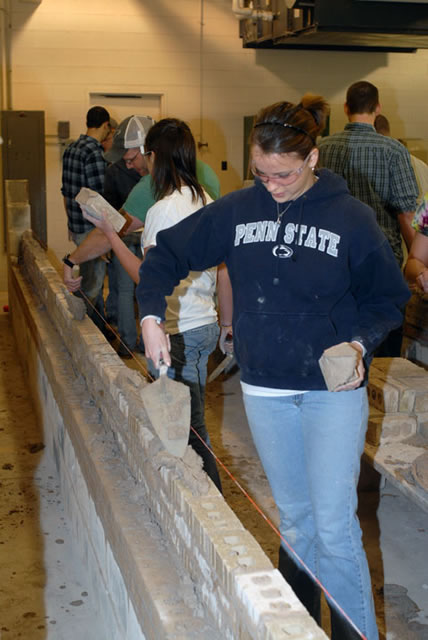 With the tools of her newfound trade in hand, a Penn State architecture major adds her stamp to a wall of bricks.