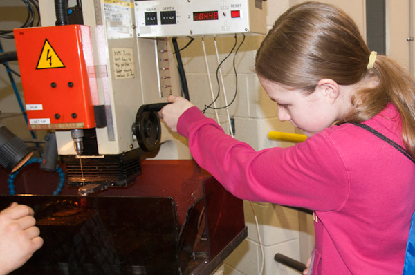 A participant uses electric discharge machining to add a hole to a metal pendant.