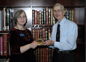 Patricia A. Scott, collection development librarian and archivist at Pennsylvania College of Technology's Madigan Library, accepts a donation from alumnus Donald W. Stout. The two hold a brass-and-steel model of a gasoline engine that Stout tooled in the Williamsport Technical Institute machine shop after his World War II service.