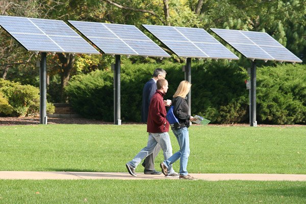With the college's solar panels and sunshine as a backdrop, Thomas E. Ask, associate professor of industrial and human factors design, leads guests along a walkway.