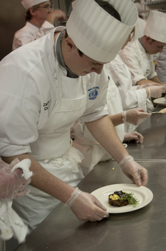 Culinary arts and systems student Zachary Derck passes a plate down the production line.