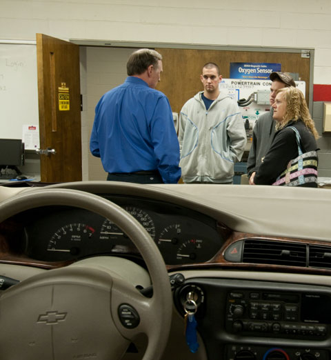 Framed by a vehicle's dashboard, Steven H. Wallace, assistant dean of transportation technology, meets with an inquisitive family in an automotive lab.
