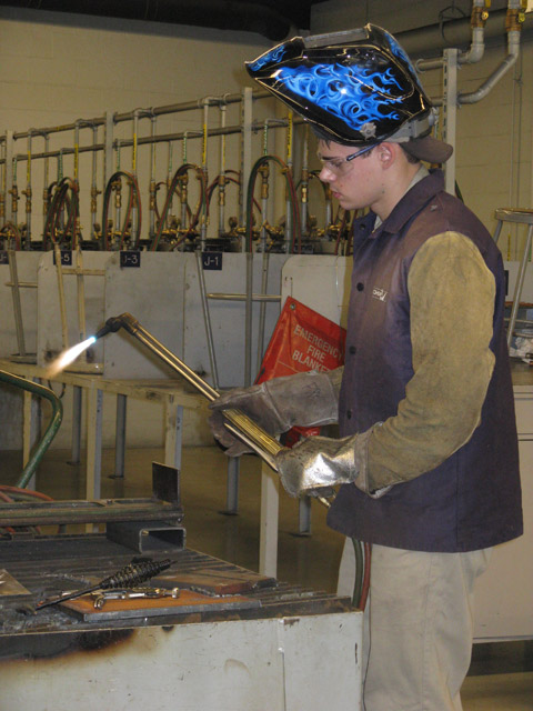 With an appropriately flame-adorned safety helmet, a student welder prepares for competition.