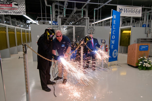 Penn College Board of Directors Chairman Robert E. Dunham and college President Davie Jane Gilmour (in welding helmets and assisted respectively by David R. Cotner, instructor of welding, and Donald O. Praster, dean of industrial and engineering technologies) sever a chain at the Metal Trades Center in lieu of a traditional ribbon-cutting.