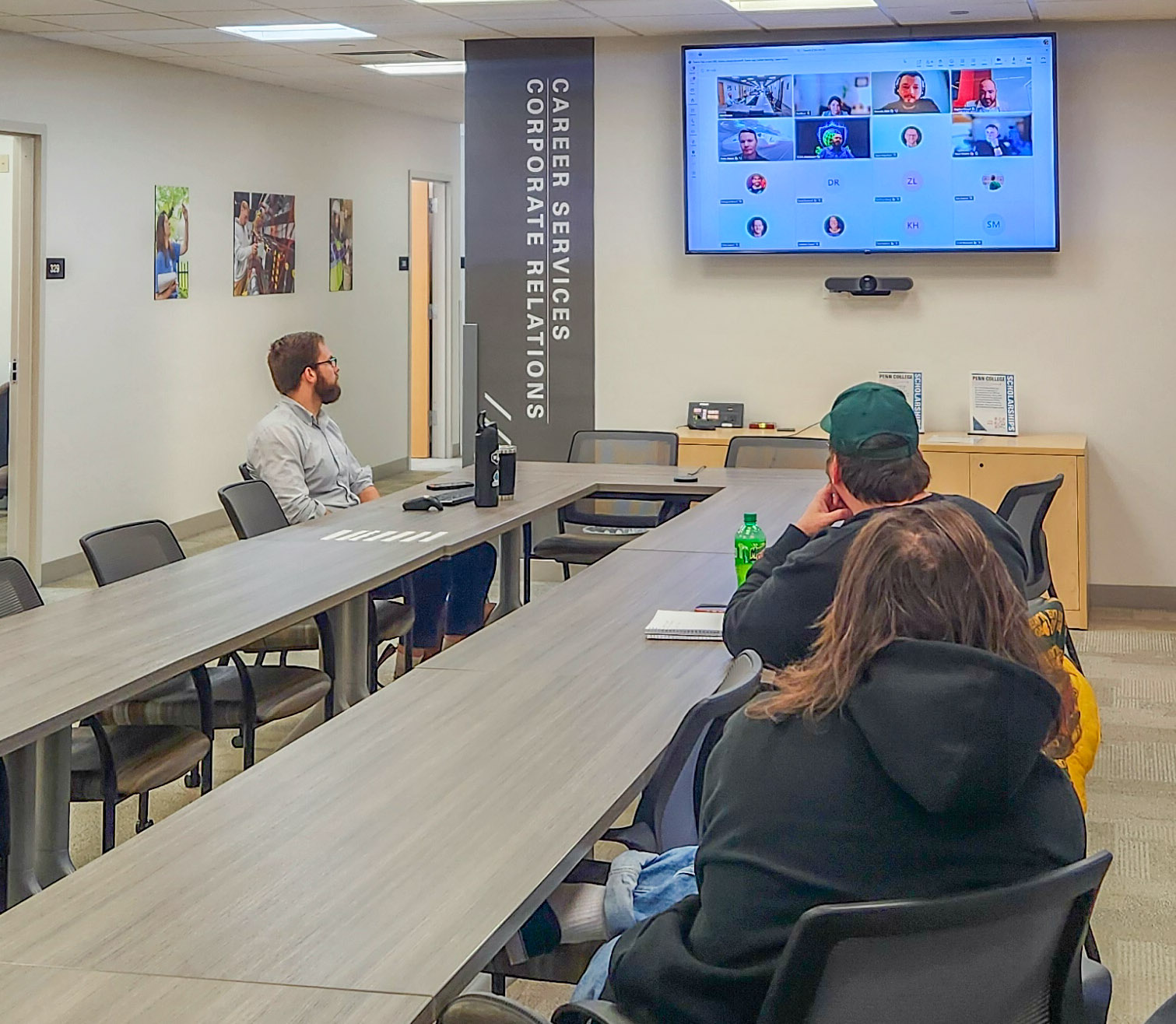 People sitting around a long table in Penn College's Center for Career Design focus on a large video screen that shows a virtual meeting in progress.