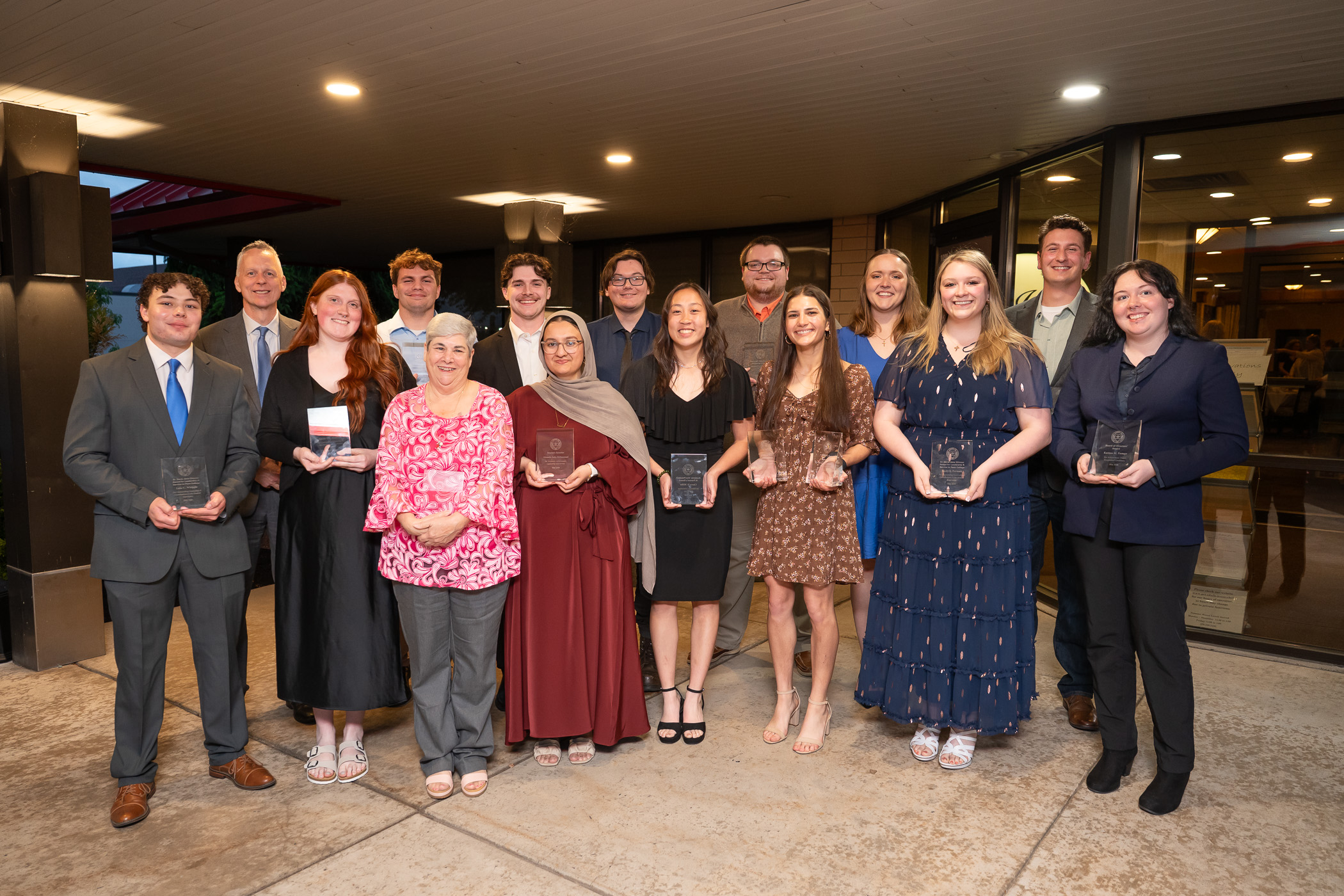 A large group of students in dressy clothes holding glass trophies.
